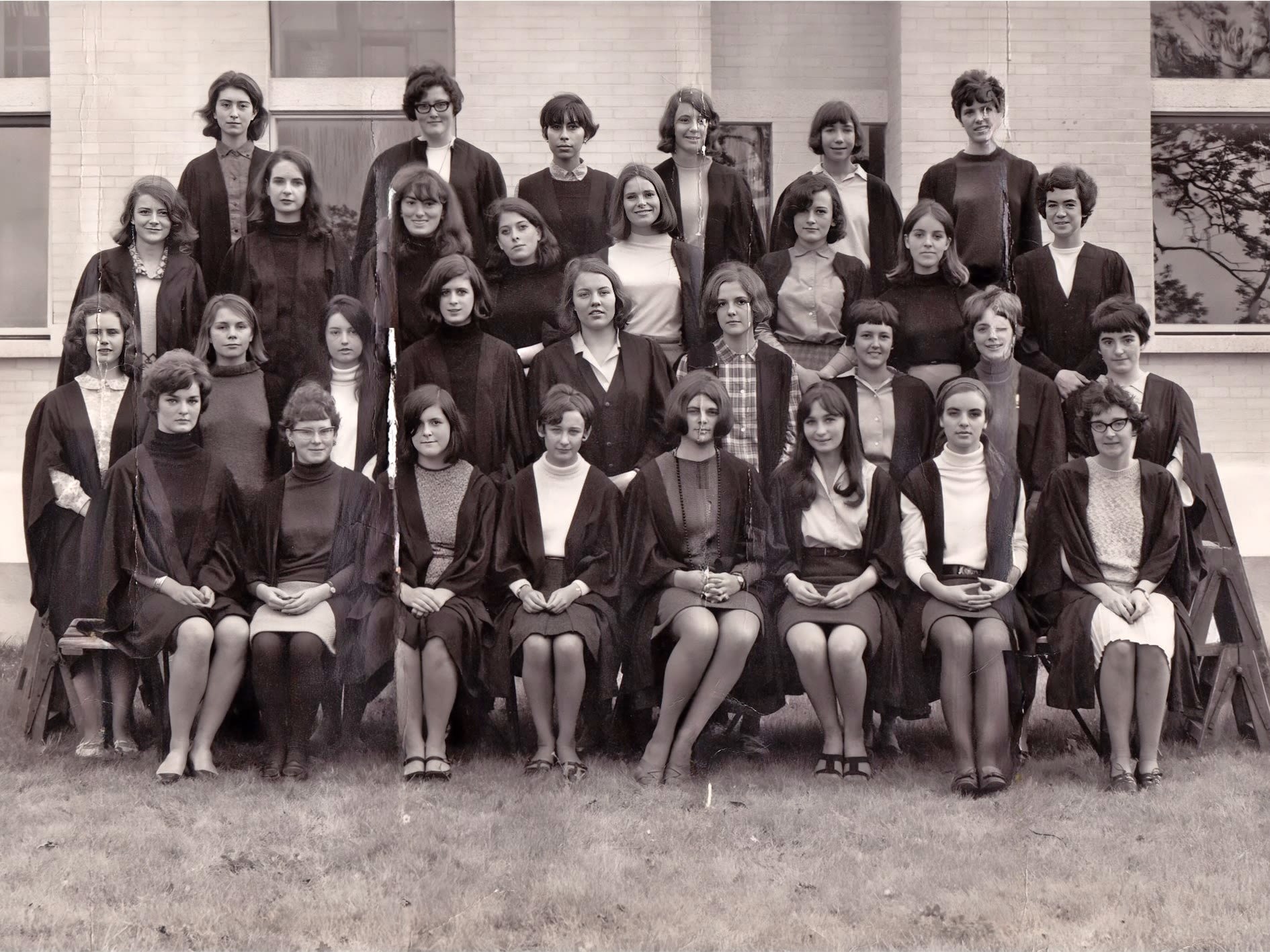 Four lines of female students are arranged for a group photo. The image is in black and white. Each where College gowns over their 1960s fashion clothes.