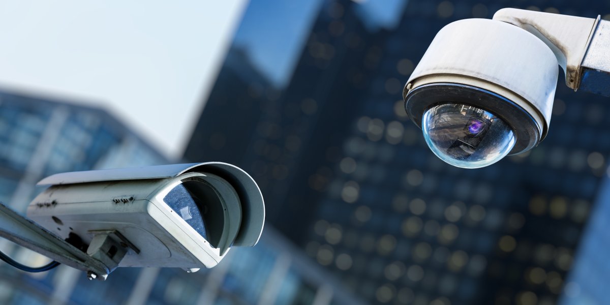 Two cctv security camera in a city with blury business building on background